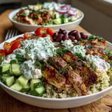 A close-up of a Greek Chicken Power Bowl showing colorful diced cucumbers, halved cherry tomatoes, and a generous dollop of homemade tzatziki sauce on warm quinoa.