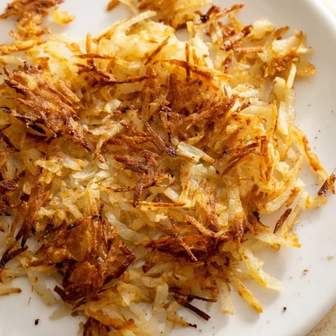 A close-up of golden-brown Hash Browns served with eggs and bacon.