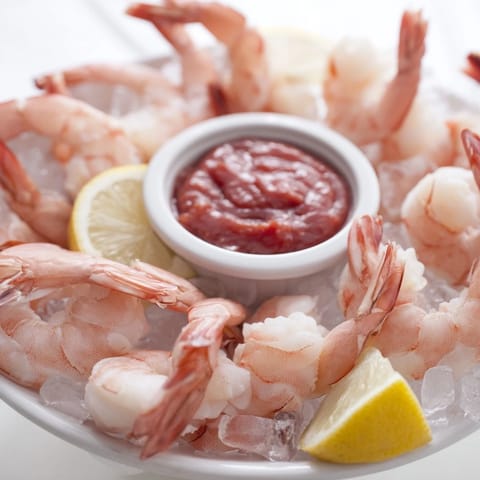 Bright red shrimp cocktail served in a glass bowl with homemade spicy sauce and a garnish of parsley.
