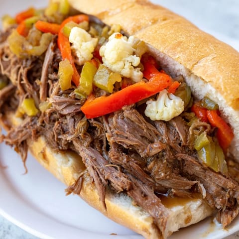 A warm Italian beef sandwich being dipped into a small bowl of savory au jus, creating a mouthwatering moment.