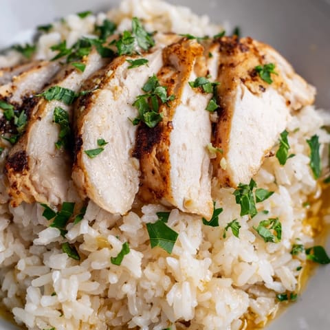 A close-up of fluffy garlic butter rice piled high, crowned with tender sliced grilled chicken and a vibrant lemon garnish.  