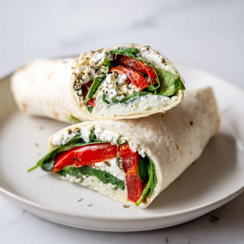 Close-up of a Mediterranean Veggie Wrap on a rustic board, featuring crumbled feta and smoky red peppers inside a soft tortilla.
