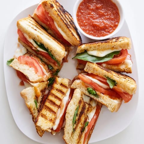 Freshly grilled Caprese Grilled Cheese Dippers on a wooden board, sliced into dippable strips beside a bowl of red marinara.