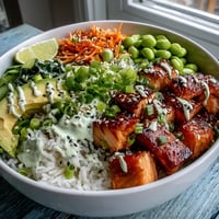 Golden-brown broiled salmon cubes rest on fluffy white rice beside crisp cucumber, shredded carrots, and creamy avocado slices in this vibrant Baked Salmon Rice Bowl.