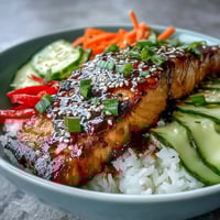 Soy-ginger glazed salmon rests on fluffy rice with crisp veggies and sesame seeds in this Asian-Inspired Salmon Bowl.